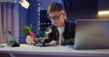 Zeki genç öğrenci evdeki fen projesinde elektronik ve lehim telleri ve devre kartlarını inceliyor. Eğitim Konsepti. Yavaş çekim.