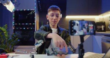 Akıllı genç vlogger kameralı telefona bakar ve podcast kaydeder. Elektronik pano tutan ve takipçilerine evini gösteren bir erkek. Eğitim ve modern teknoloji kavramı. Yavaş çekim.
