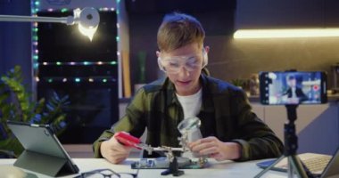 Çocuk vlogger akıllı telefonu kullanarak online yayın yapıyor. Bilim projesinde elektronik aletler ve lehimleme kabloları ve devre kartları okuyor ve takipçilere evde öğretiyor. Yavaş çekim
