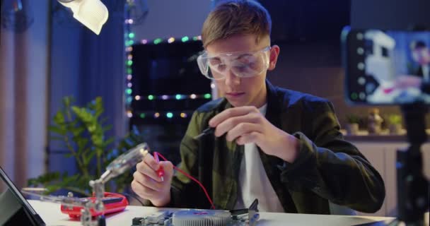道具を持った眼鏡の白人の少年は 家庭用電子機器を修理する 男性プロの少年がコンピュータを修理する エンジニアはんだ付け回路 スローモーション — ストック動画