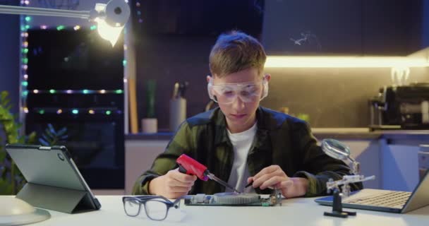 可爱的笑容 一个戴着防护眼镜的少年 用焊铁和摄像头固定小细节 电脑的业余爱好概念 慢动作 — 图库视频影像