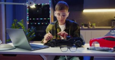 Akıllı çocuk akşam odasında masa başında bir araba oyuncağını tamir ediyor. Evde robot araba ödevi projesi. Ev işleri kavramı, bağımsız çocuk. Yavaş çekim.