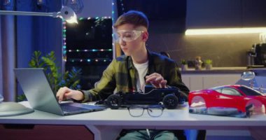Genç çocuk dizüstü bilgisayarından izlediği bir videoya göre oyuncak otomobil montajı için somunu tornavidayla sıkıyor ve elektronik yapay zeka atölyesi dersi veriyor. Gelişmiş hobiler