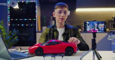 Genç çocuk vlogger, akıllı telefon kullanarak elektrikli devre binası ve arabaları akşam evde monte etme ve test etme ile ilgili video kaydediyor. Yavaş çekim.