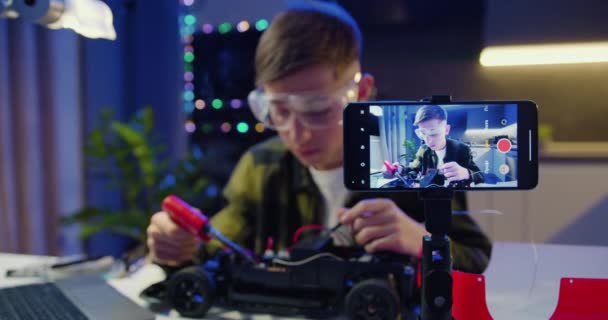 少年坐在办公桌前 戴着安全护目镜 培养了他对焊锡的热情 Vlogger让使用智能手机的在线流媒体教他们如何使用焊料和工具 慢动作 — 图库视频影像