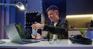 Ergen, akşam evde akıllı telefondan video oyunu oynuyor. Çocuk oyun oynamak için telefonu kullanıyor. Oyuncu cep telefonu kullanıyor ve oyun oynuyor. Yavaş çekim.