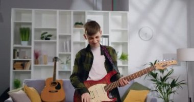 Kafkasyalı genç çocuk dans ediyor, gitar çalıyor ve oturma odasında müzik dinliyor. Mutlu ve çılgın, eğleniyor. Yavaş çekim.
