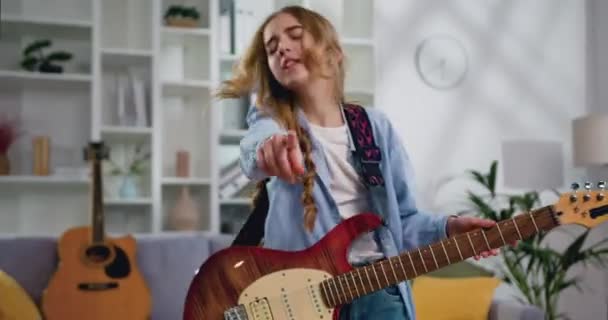 リビングルームで魅力的な女の子のダンス 十代の女性が家の中で楽しい気分でギターを弾く 自宅のリビングルームで楽しい時間を過ごしています — ストック動画