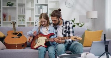Baba ve kızı öğretmenlik yapıyor, gitar çalıyor ve evde notalar öğreniyor. Yetenekli özel öğretmen küçük öğrencisine gitar çalmayı öğretiyor. Yavaş çekim.