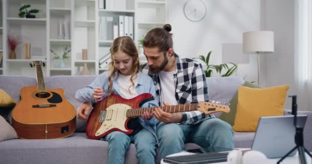 父亲和女儿在家里教书 弹吉他和学习音乐笔记 熟练的个人导师教他的小学生弹吉他要好 慢动作 — 图库视频影像