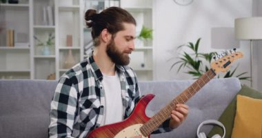 Fotoğraftaki gülümseyen çocuk kameraya bakıyor. Avrupalı erkek, ev stüdyosunda dizüstü bilgisayarla elektro gitar öğreniyor. E-öğrenme, çevrimiçi eğitim kavramı.