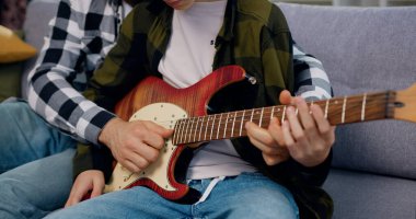 Gitarcı çocuk gitar çalmayı öğreten sevimli çocuğa yardım ediyor. Babam modern odada kanepede oturup birlikte öğreniyor..