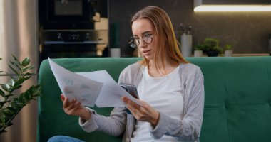 Evinde kağıt belgelerle çalışan ve evde akıllı telefon kullanan genç bir kadın. Serbest çalışan ya da uzaktan eğitim gören bir kız. Mesafe öğrenme ve iş kavramı.