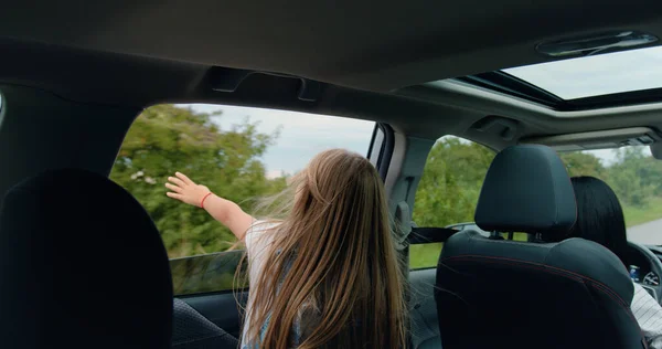 Hareket halindeki arabanın içinden çekilen 12 yaşındaki güzel sarışın kız kafasını ve elini araba camından dışarı uzatıyor ve doğa ve esintiye hayran kalıyor.