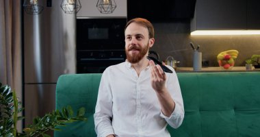 Attaractive man sit in kitchen hold smart phone talk on speakerphone. Male recording audio message for friends or partners, sharing news using mobile phone application.