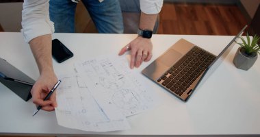 Üst Manzara. Büyük kağıt format şeması üzerinde kalem çizgileri tutan, mühendislik masasında çalışan, konsantre olan ve plan çizen insan elleri.