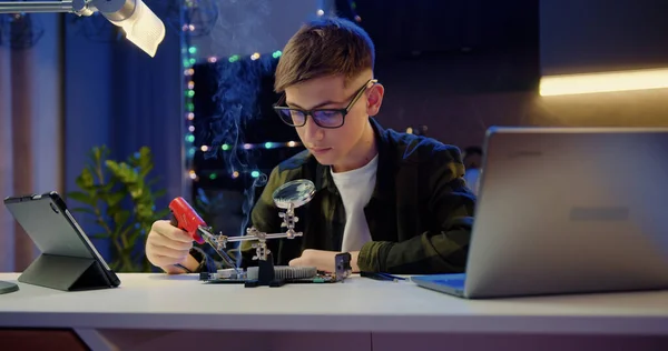 スマート十代の少年は自宅で彼の科学プロジェクトで電子機器やハンダ付けワイヤや回路基板を研究しています 教育理念 — ストック写真