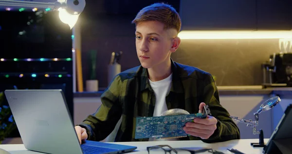 魅力的な現代のティーン男の子で保護ガラス彼の手でコンピュータボードを考慮し ノートパソコンの画面上でその構造の指示を読む — ストック写真