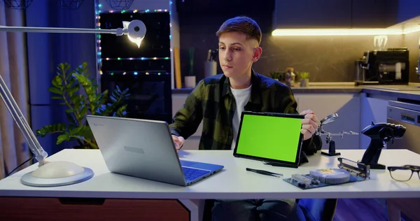 ラップトップ作業を使用して魅力的な少年は コールビデオ会議を持っています ティーンエイジャーは コールビデオ会議中に緑色の画面を持つタブレットを示しています クロマキーテクノロジー マーケティングデザインコンセプト — ストック写真