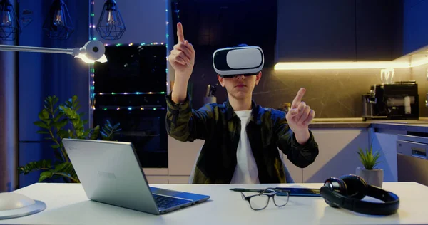 十几岁的男孩戴着Vr眼镜 手牵手在空气中翻动打字 坐在客厅的桌子上 虚拟现实 现代小玩意装置 — 图库照片