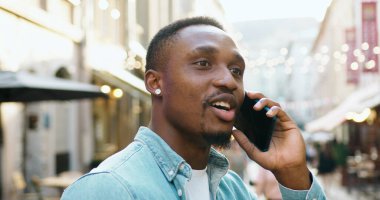 Çekici, dost canlısı, neşeli, siyah derili, şık sakallı genç adam yaz mevsiminde, sokakta rahat sokak kafeleriyle yürürken telefonla konuşmaktan zevk alıyor.