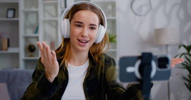 Kadın nüfuzlu blogcu, kulaklıklı çekici genç kız sosyal medya için video bloğu çekiyor ve konuşuyor, cep telefonu kullanıyor..