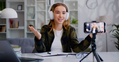 Gülümseyen yetenekli kadın blogcu internet izleyicileri için video kaydediyor ve modern oturma odasında alkışlıyor..