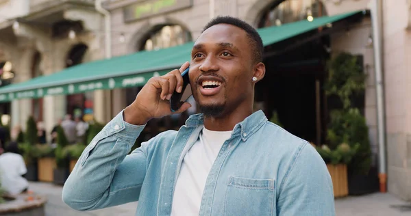 stock image Handsome in high spirits modern young stylish dark-skinned man enjoying his positive mobile conversation near beautiful street cafe at daytime in summer,close up