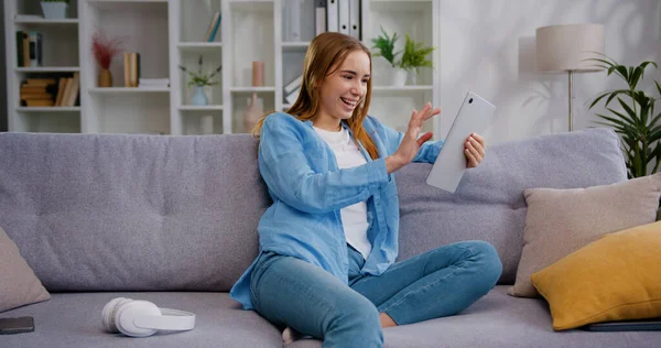 Oldukça mutlu gülümseyen Kafkasyalı genç bir kadın rahat bir koltukta oturuyor, dijital tablet internet çalışması yapıyor sosyal medya uygulamaları kullanarak online alışveriş yapıyor ya da evde oyun oynuyor..