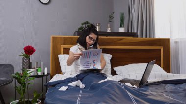 Hasta, yorgun bir kadın yatak odasında oturup telefonda konuşurken grip salgını sırasında mali raporları gözden geçirir, uzaktan evde çalışır.