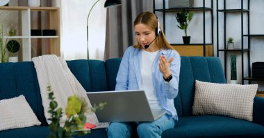 İyi halden oldukça emin kulaklıklı genç, açık renk saçlı kız evden bir arkadaşıyla video görüşmesi yapıyor ve akıllı saat üzerindeki zamanı kontrol ediyor.