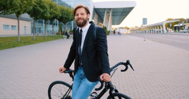 Etkileyici güzel havaalanı arka planında ya da başka bir binada bisikletinin üstünde poz veren yakışıklı, modern, sakallı bir adam.