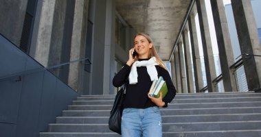 Sevimli, gülümseyen, gündelik giysiler içinde üniversite binasından ders kitaplarıyla merdivenlerden inen ve telefon sohbetinin keyfini çıkaran sevimli, zeki bir genç kız.