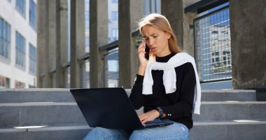 Şehir binasının beton merdivenlerinde dinlenen, hareketli sohbetler sırasında dizüstü bilgisayardaki bilgileri değiştiren, modaya uygun 25 yaşında genç bir kadının portresi.