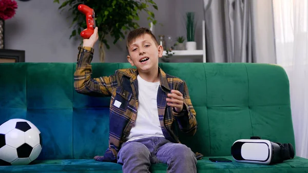 Çağdaş dairede yeşil yumuşak koltukta oturan ve oyun oynayan, gündelik giysiler içindeki yakışıklı, duygusal çocuk.