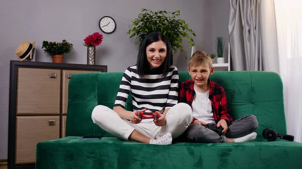 魅力的な幸せな攪拌笑顔母と息子のフロントビュー ソファに座って ジョイスティックを使用してビデオゲームをプレイ — ストック写真
