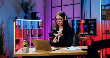 Güzel, kendine güvenen, stil sahibi, koyu renk saçlı, kulaklıklı bir iş kadınının çalışanlarıyla internet üzerinden toplantı yaptığı bir iş konsepti.