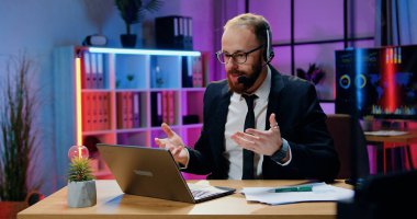 Müşterilerle video görüşmesi yaparken kulaklık takan, resmi gözlüklü, başarılı, deneyimli, modern, sakallı ofis yöneticisi konsepti