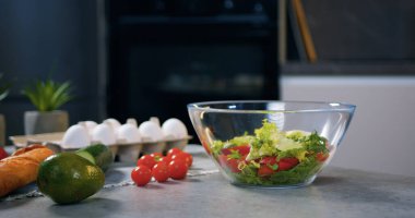 Vitamin salatasına hazırlanmış vişneli domateslerin olduğu şeffaf kâseye düşen taze, besleyici, küçük marul parçaları.