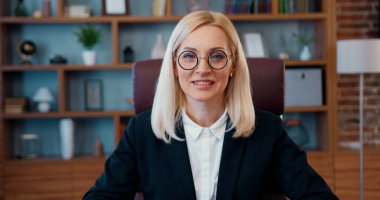 Resmî iş dünyasındaki sevimli gülümseyen, yetenekli kadın ofis müdürü. Önce pencereye bak, sonra da modern, iyi donanımlı bir dolapta, iş portresinde poz ver.