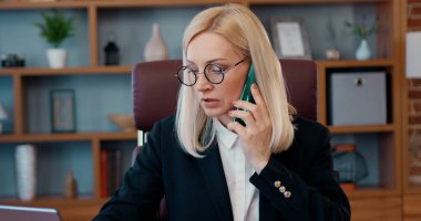 Belgeler ve dizüstü bilgisayarlarla çalışan kendine güvenen güzel bir iş kadını aynı anda modern ofis ve cephede iş görüşmeleri yapıyor.