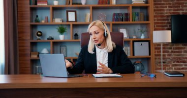 Güzel görünüşlü, kendine güveni tam başarılı bir iş kadını. Kulaklığı bilgisayarında iş arkadaşlarıyla video konferansı düzenliyor ve iş konularını tartışıyor.