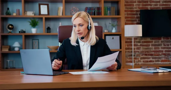 Bilgisayarda iş arkadaşlarıyla iş görüşmesi yapan ve ortak iş konularını tartışan kulaklıklı çekici, kendine güvenen başarılı sarışın kadın ofis müdürünün portresi.