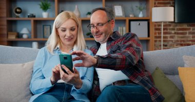 Mutlu mutlu, mutlu, evli bir çift evdeki kanepede dinleniyor ve akıllı telefon uygulamalarında sörf yapıyor, aile eğlencesi konsepti.