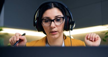 Gözlüklü, 35 yaşında, başarılı, siyah saçlı, kendine güveni tam bir kadın. Ev bilgisayarında online video konferansı düzenliyor.