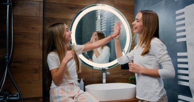 Kafkasyalı genç ve kız kardeşler dişlerini fırçalarken birbirlerine gülümserken bakıyorlar. Gülümseyen kadın ve çocuk sabah diş sağlığıyla ilgileniyorlar..