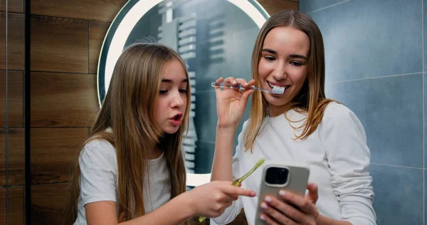 Young Happy Smiling Girls Using Smartphone While Brushing Her Teeth — Stock Photo, Image