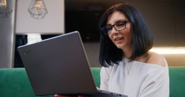 Kanepede oturan ve dizüstü bilgisayar, çalışma, blog yazma ve sohbet kullanarak proje üzerinde çalışan serbest çalışan kadın portresi. Genç bir kadın arkadaşlarıyla uzaktan konuşmak için dizüstü bilgisayar kullanıyor.