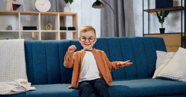 Yakışıklı, mutlu, gözlüklü, şık giyinmiş, rahat koltukta oturmuş, tatmin olmuş bir şekilde kameraya bakan iki yaşında bir çocuk.