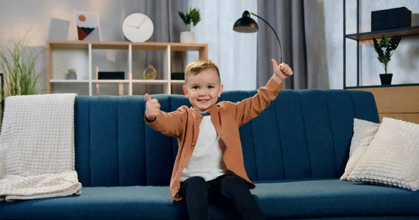 Sevimli, mutlu, gülümseyen, 2 yaşında bir çocuk. Çağdaş odada kanepede oturuyor ve fotoğraf makinesine şöyle yazıyor: